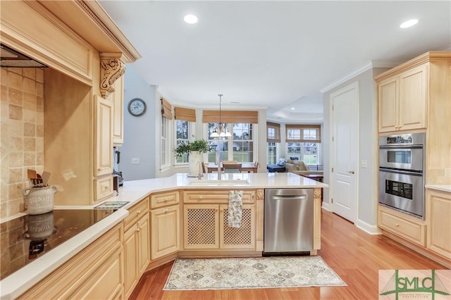 kitchen featuring pendant lighting, stainless steel appliances, light countertops, light wood-style flooring, and a sink