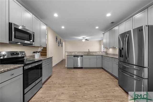 kitchen with light wood-style flooring, gray cabinetry, appliances with stainless steel finishes, a sink, and dark stone countertops