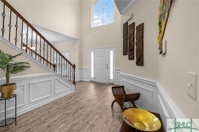 entrance foyer featuring a decorative wall, stairway, ornamental molding, wainscoting, and wood finished floors