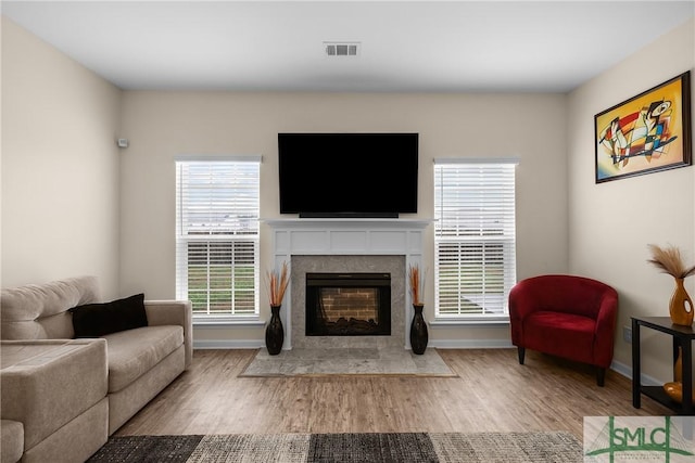 living area featuring light wood-type flooring, a fireplace with flush hearth, visible vents, and baseboards