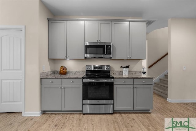 kitchen with appliances with stainless steel finishes, light wood-type flooring, gray cabinets, and light stone counters