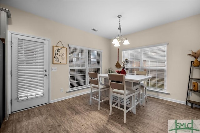 dining space featuring baseboards, wood finished floors, visible vents, and a notable chandelier