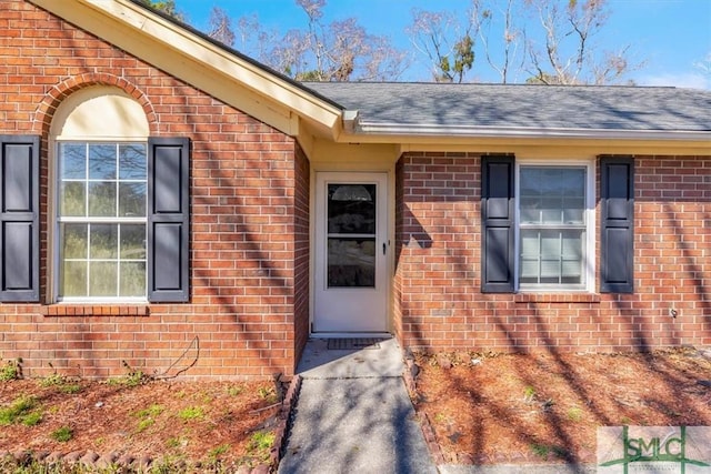 entrance to property with a shingled roof and brick siding