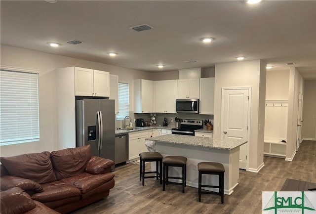 kitchen with light stone counters, stainless steel appliances, a sink, a kitchen island, and a kitchen breakfast bar