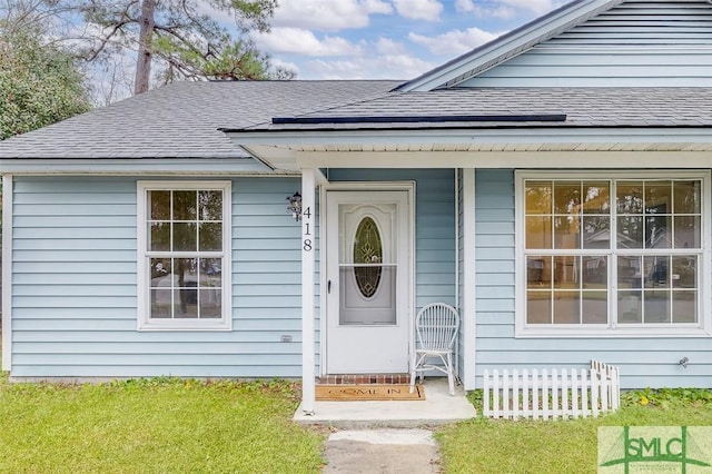 view of exterior entry with a lawn and roof with shingles