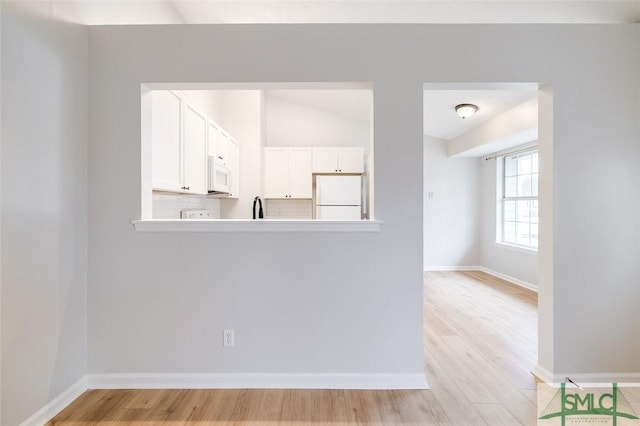 unfurnished room with vaulted ceiling, light wood-style flooring, and baseboards