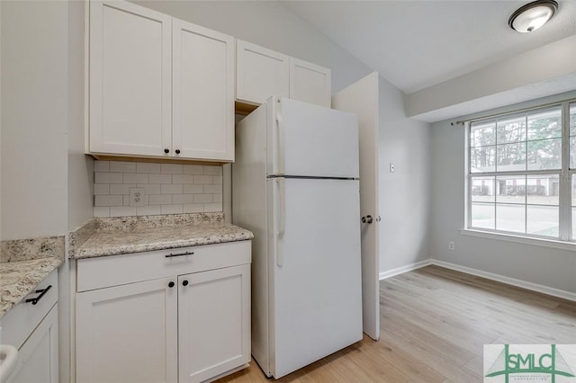 kitchen featuring light stone counters, white cabinetry, freestanding refrigerator, decorative backsplash, and light wood finished floors