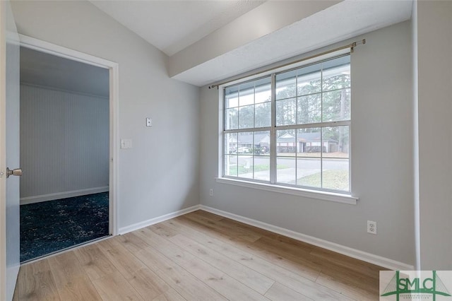 spare room with lofted ceiling, light wood finished floors, and baseboards