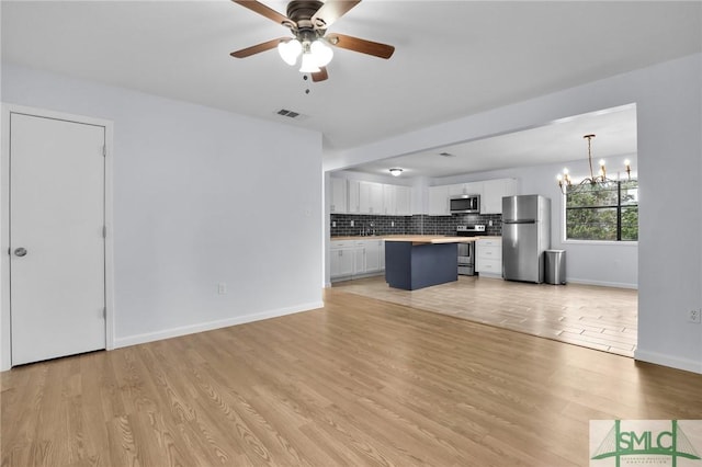 unfurnished living room with ceiling fan with notable chandelier, light wood finished floors, visible vents, and baseboards