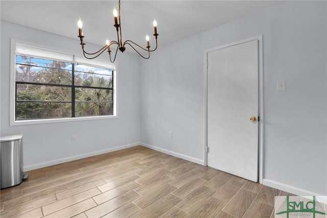 unfurnished dining area with an inviting chandelier, baseboards, and wood finish floors