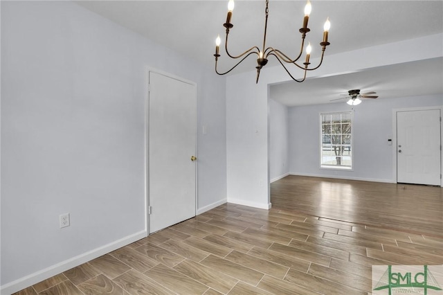 unfurnished dining area featuring wood tiled floor, baseboards, and ceiling fan with notable chandelier