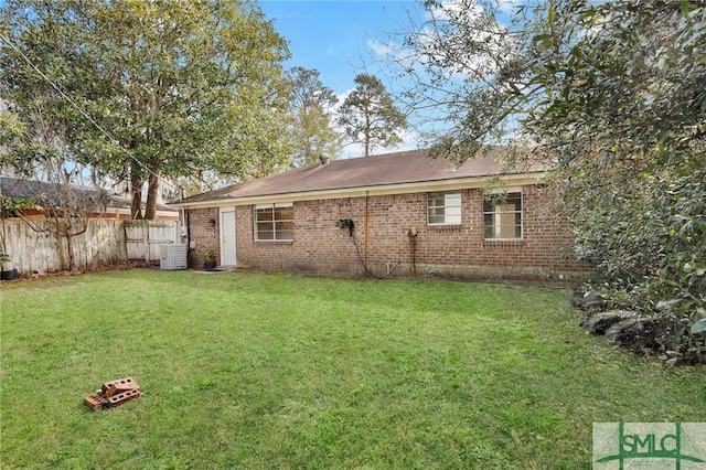 rear view of house with cooling unit, brick siding, fence, and a lawn