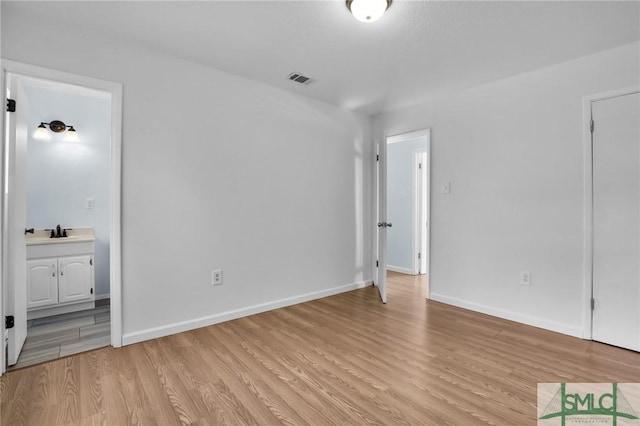 unfurnished bedroom with connected bathroom, a sink, visible vents, baseboards, and light wood-type flooring