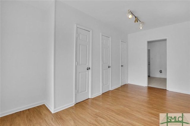 unfurnished bedroom with multiple closets, light wood-type flooring, and rail lighting