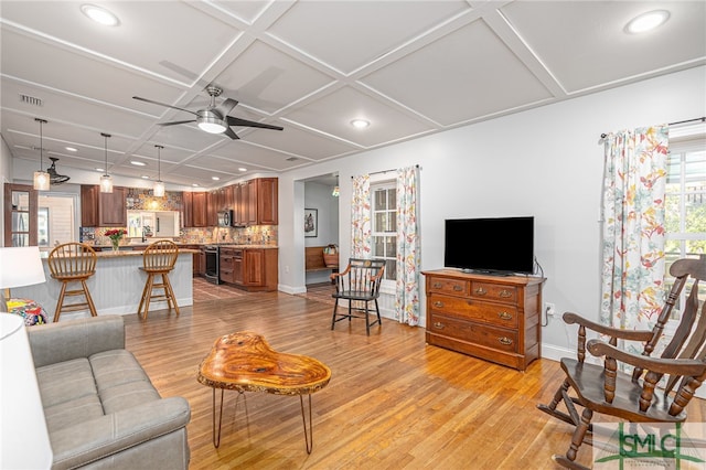 living room featuring ceiling fan, light wood-type flooring, coffered ceiling, and baseboards