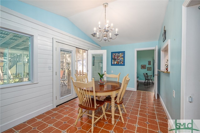 dining space with lofted ceiling, wooden walls, baseboards, and an inviting chandelier