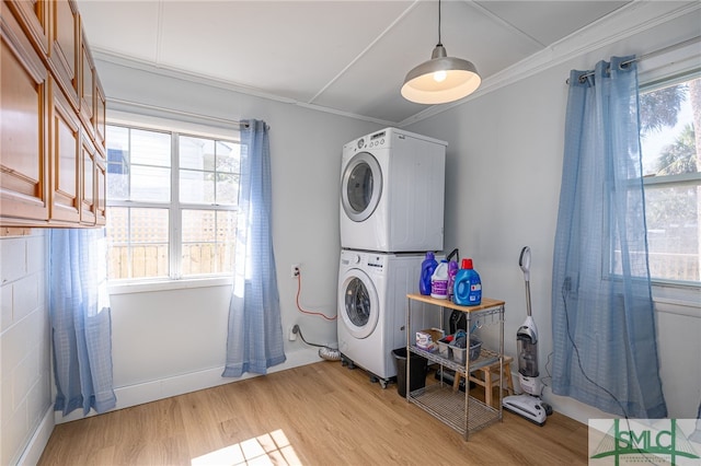 laundry area with light wood-type flooring, stacked washing maching and dryer, laundry area, and crown molding