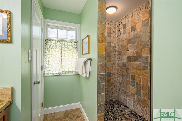 bathroom with baseboards, tiled shower, and vanity