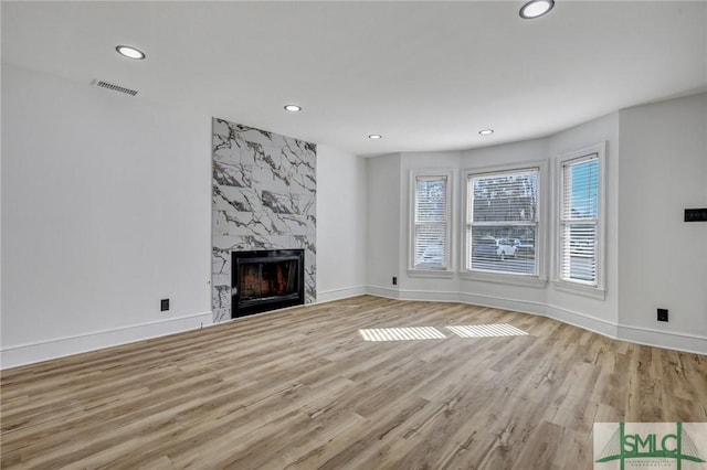 unfurnished living room with recessed lighting, visible vents, a premium fireplace, light wood-type flooring, and baseboards