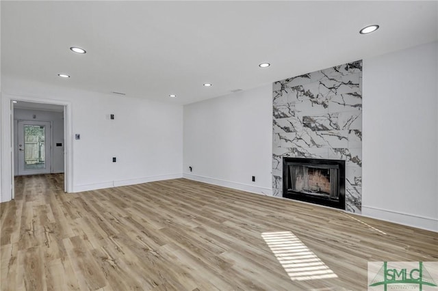 unfurnished living room featuring light wood finished floors, recessed lighting, baseboards, and a high end fireplace