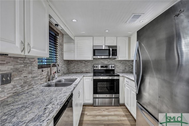 kitchen featuring a sink, white cabinetry, appliances with stainless steel finishes, backsplash, and light stone countertops