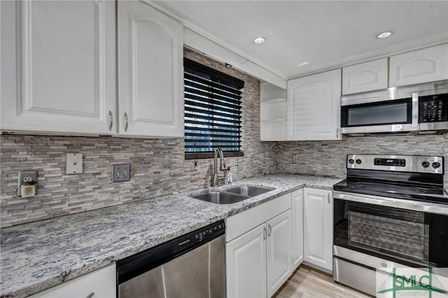 kitchen with light stone countertops, white cabinetry, stainless steel appliances, and a sink