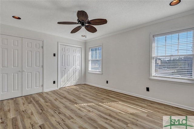 unfurnished bedroom with a ceiling fan, baseboards, light wood-style floors, ornamental molding, and two closets