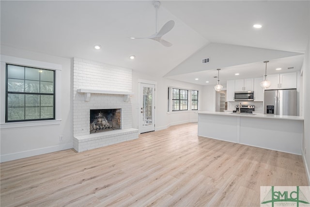 unfurnished living room featuring lofted ceiling, a fireplace, visible vents, a ceiling fan, and light wood-style floors