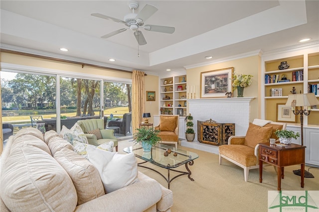 living area with built in features, a tray ceiling, a fireplace, recessed lighting, and ornamental molding