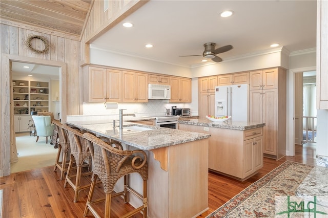 kitchen with light stone counters, white appliances, a sink, and light brown cabinetry