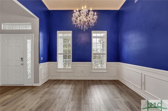 foyer entrance featuring light wood-style floors, a wainscoted wall, a notable chandelier, and crown molding