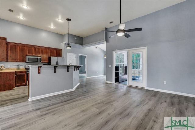 kitchen with a high ceiling, a kitchen breakfast bar, open floor plan, hanging light fixtures, and appliances with stainless steel finishes