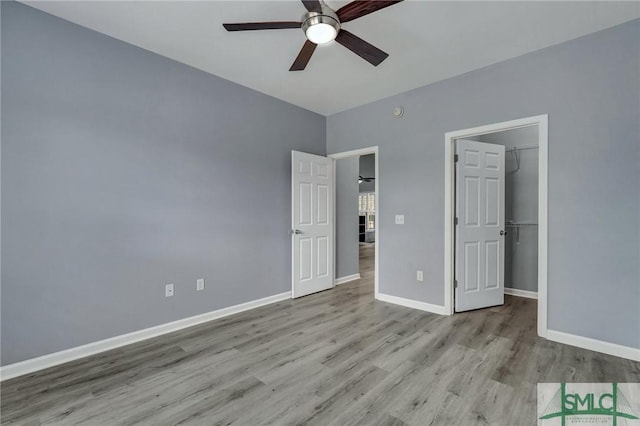 unfurnished bedroom featuring light wood-style floors, ceiling fan, a spacious closet, and baseboards