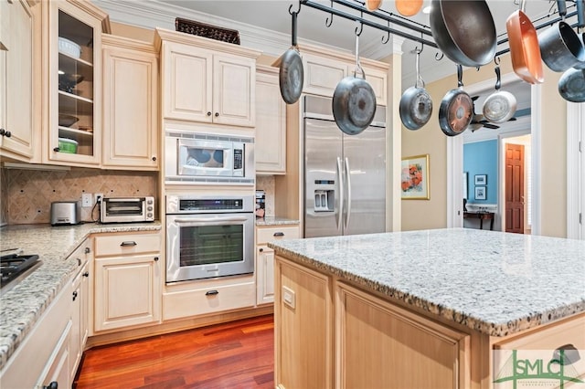 kitchen with light stone counters, tasteful backsplash, glass insert cabinets, wood finished floors, and built in appliances