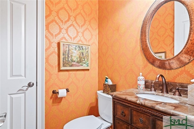 bathroom featuring vanity, toilet, and wallpapered walls