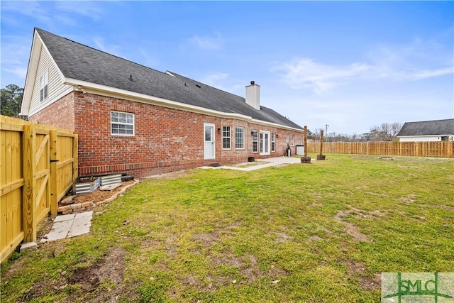 rear view of house with brick siding, a chimney, a fenced backyard, and a lawn