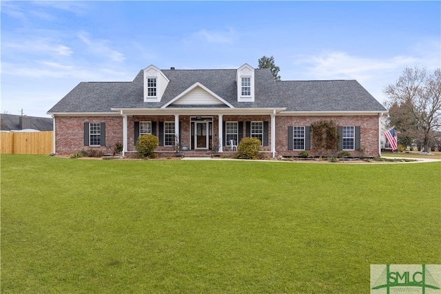 cape cod-style house featuring covered porch, brick siding, a front yard, and fence