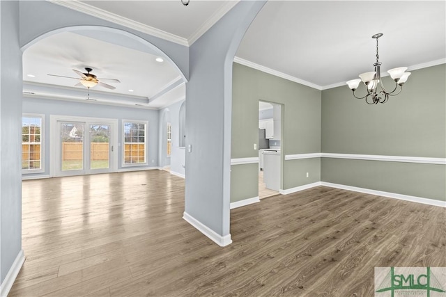 interior space with arched walkways, crown molding, wood finished floors, baseboards, and ceiling fan with notable chandelier