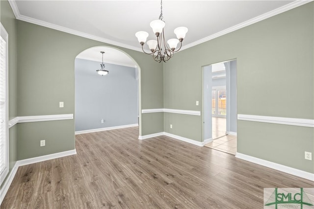 empty room featuring baseboards, arched walkways, ornamental molding, wood finished floors, and an inviting chandelier