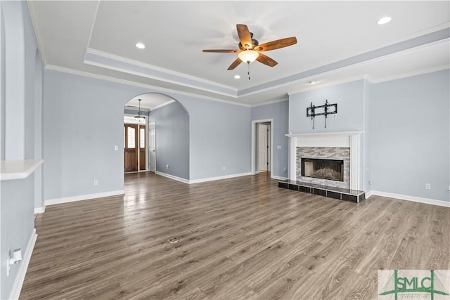 unfurnished living room with arched walkways, a raised ceiling, a tiled fireplace, and wood finished floors