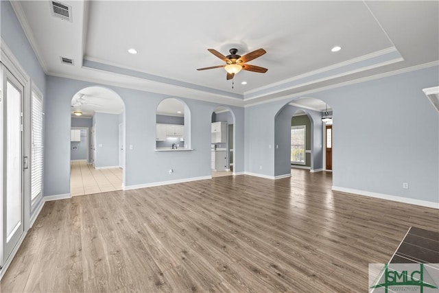 unfurnished living room with ceiling fan, visible vents, a raised ceiling, and arched walkways