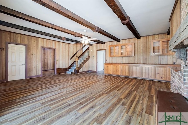 unfurnished living room with ceiling fan, dark wood-style flooring, beamed ceiling, and stairs