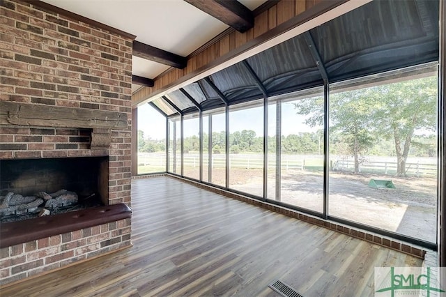 unfurnished living room with a fireplace, wood finished floors, a sunroom, beam ceiling, and floor to ceiling windows