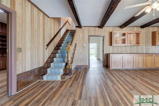 interior space with ceiling fan, wood walls, wood finished floors, stairs, and beam ceiling