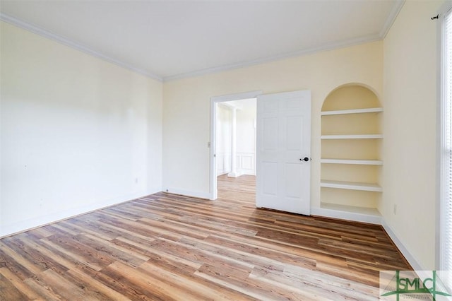 spare room featuring light wood-style floors, built in shelves, baseboards, and crown molding