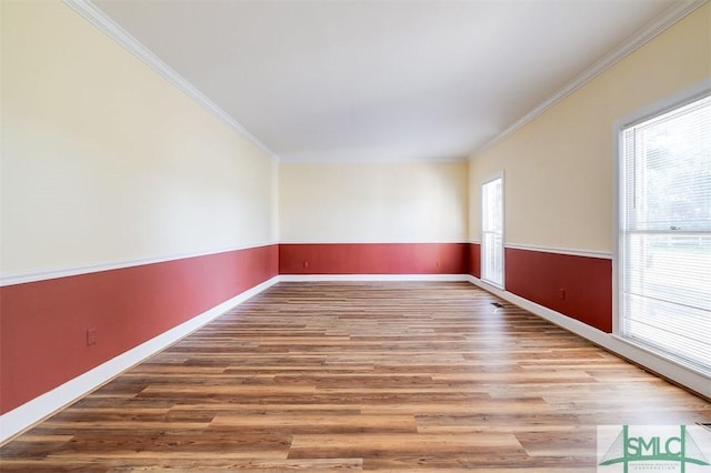 spare room with ornamental molding, wainscoting, baseboards, and wood finished floors