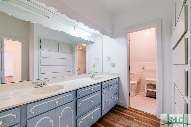 full bathroom with double vanity, toilet, ornamental molding, a sink, and wood finished floors