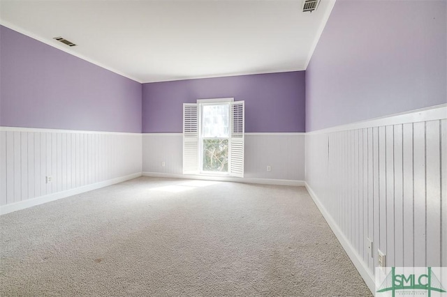 spare room featuring carpet, wainscoting, visible vents, and crown molding