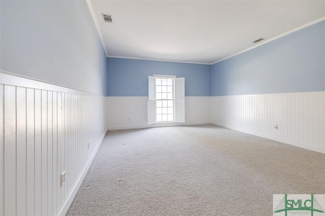 spare room featuring ornamental molding, visible vents, light colored carpet, and wainscoting