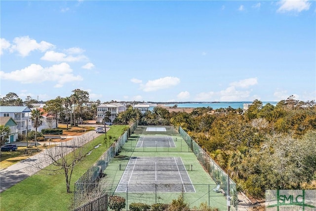 view of tennis court featuring a water view and fence